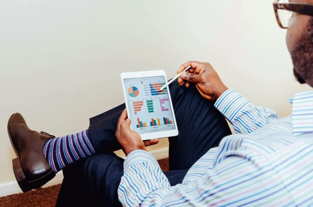 Closeup of a man sitting down using a stylus on a table or an iPad to interact with reporting charts on the screen.