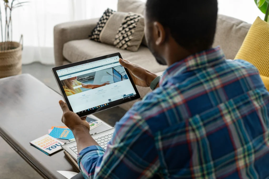 A young man sitting in front of a coffee table, holding a large tablet or iPad with a web page on the screen. How to Generate Real Estate Leads With LinkedIn.