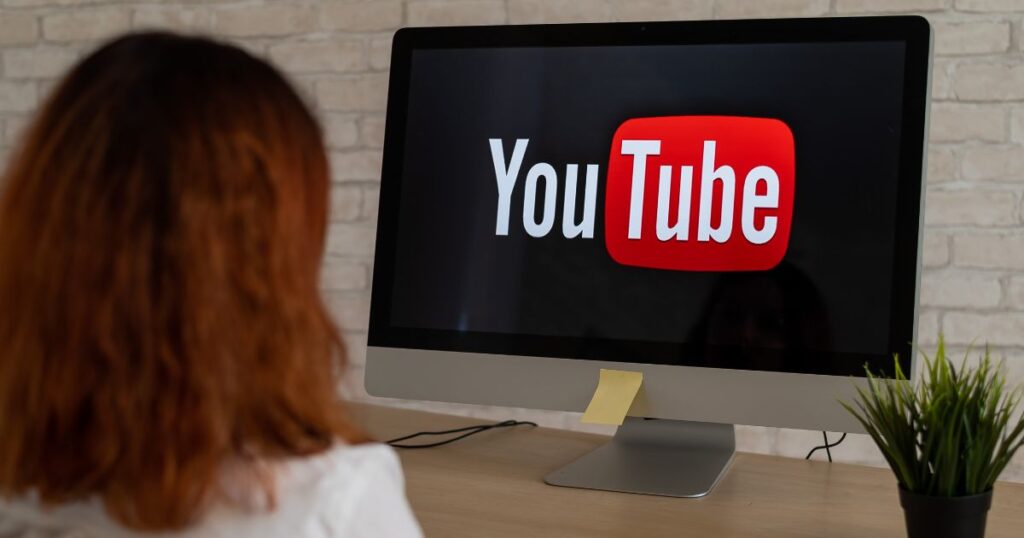 Woman looking at a computer monitor with a large YouTube logo on the screen.