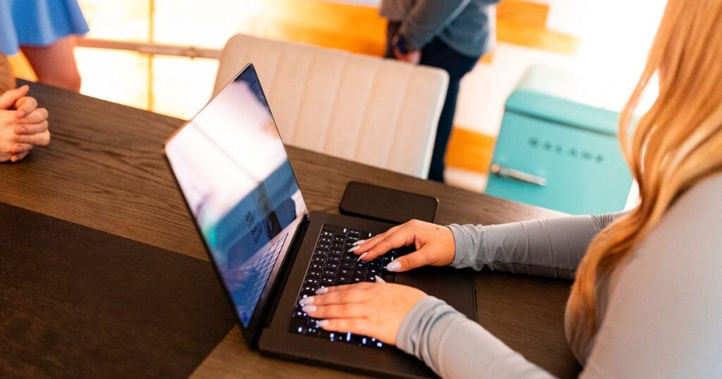 Closeup of a woman seated at a table and typing on a laptop keyboard.