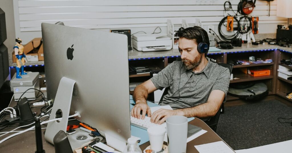 Myrddin wearing headphones and typing on a computer keyboard.