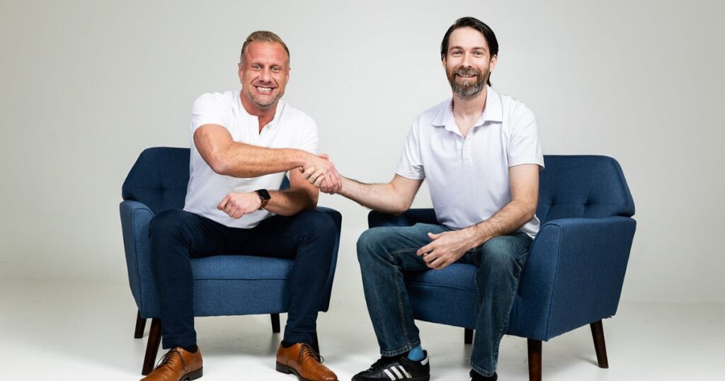 Matt and Myrddin of Two Brothers sitting on chairs next to each other and shaking hands.
