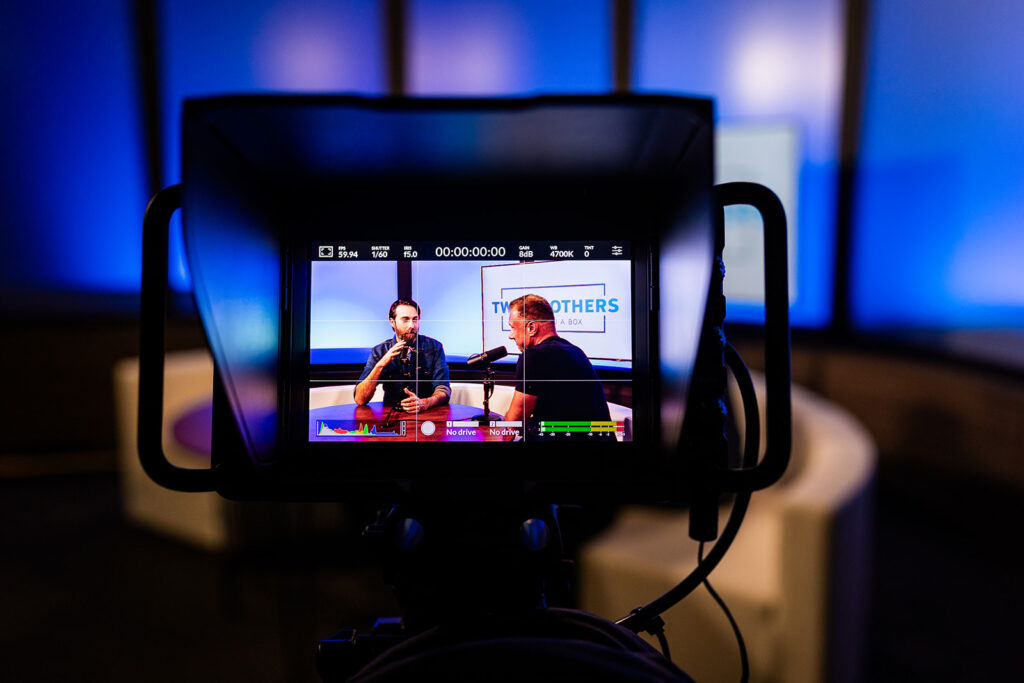 A podcast recording session seen on a camera view screen.