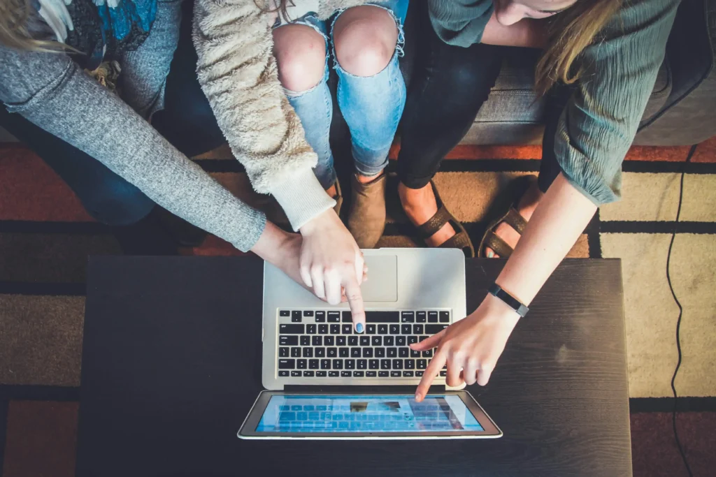 Overhead view of three young women pointing at information on a laptop screen. How to caption a real estate post on Instagram.