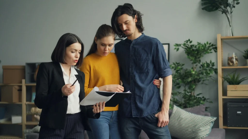 A woman in business attire showing paperwork to a young man and woman standing next to her.
