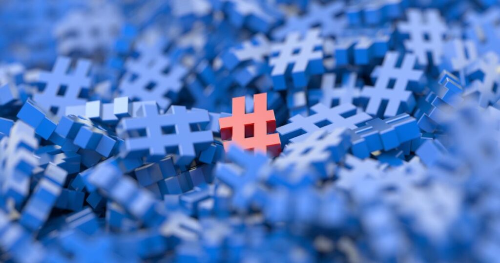 Closeup of a pile of 3-D blue hashtags with a single 3-D red hashtag in the middle of them.