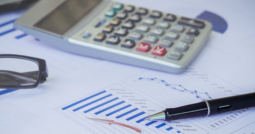 Closeup of a printout a bar chart and a line graph, caculator, eyeglasses, and a pen.