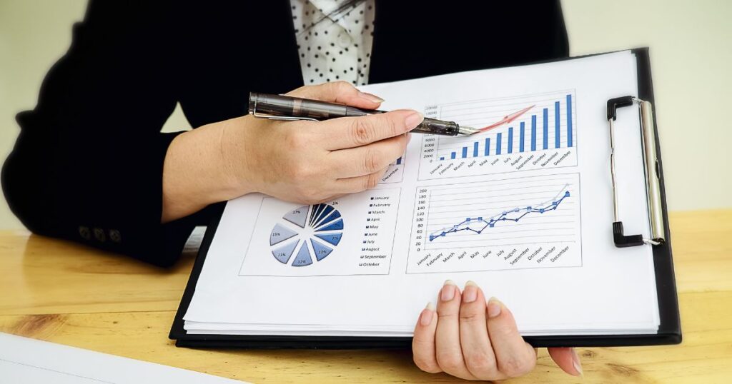 Closeup of a woman using a pen to point to a bar chart on the clipboard she is holding.