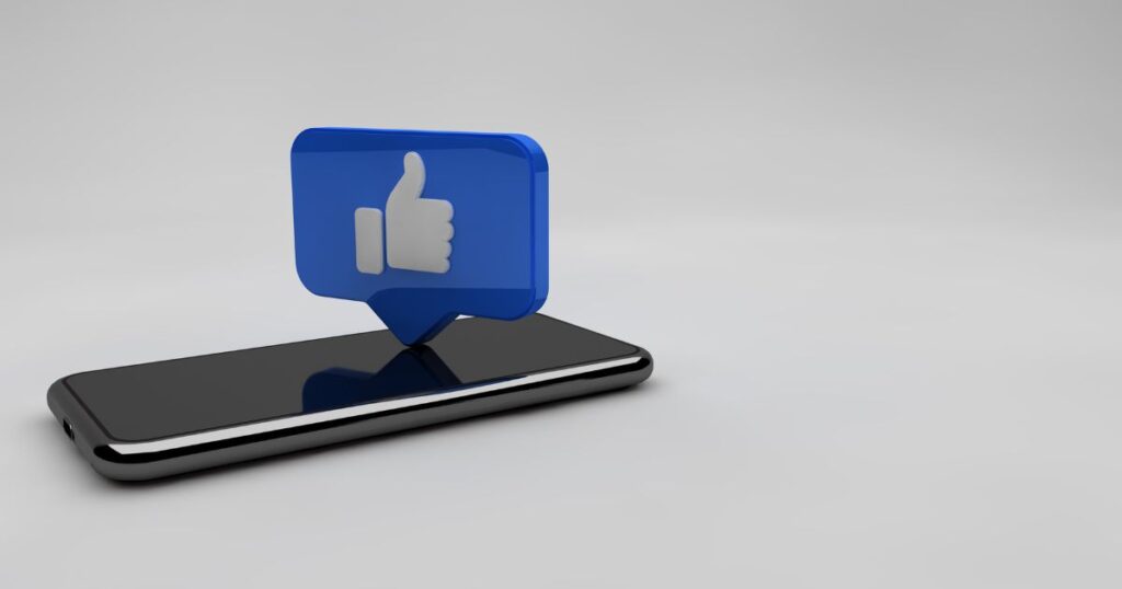 A smartphone lying on a horizontal surface with a blue Facebook Like icon above the screen.