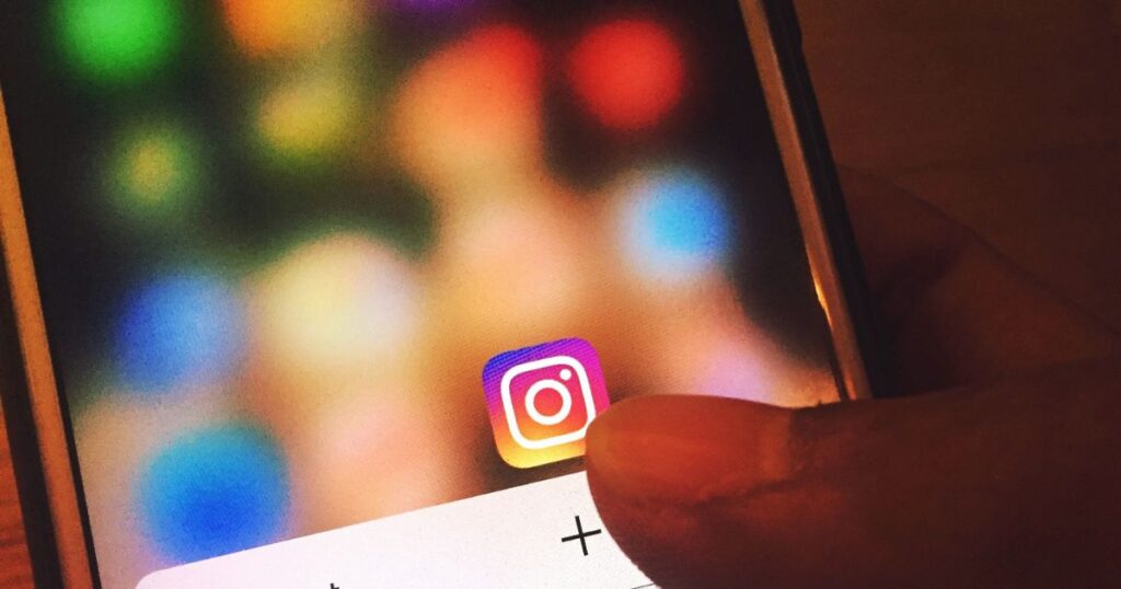 Closeup of a person's thumb clicking on a plus sign for Instagram on a smartphone screen.