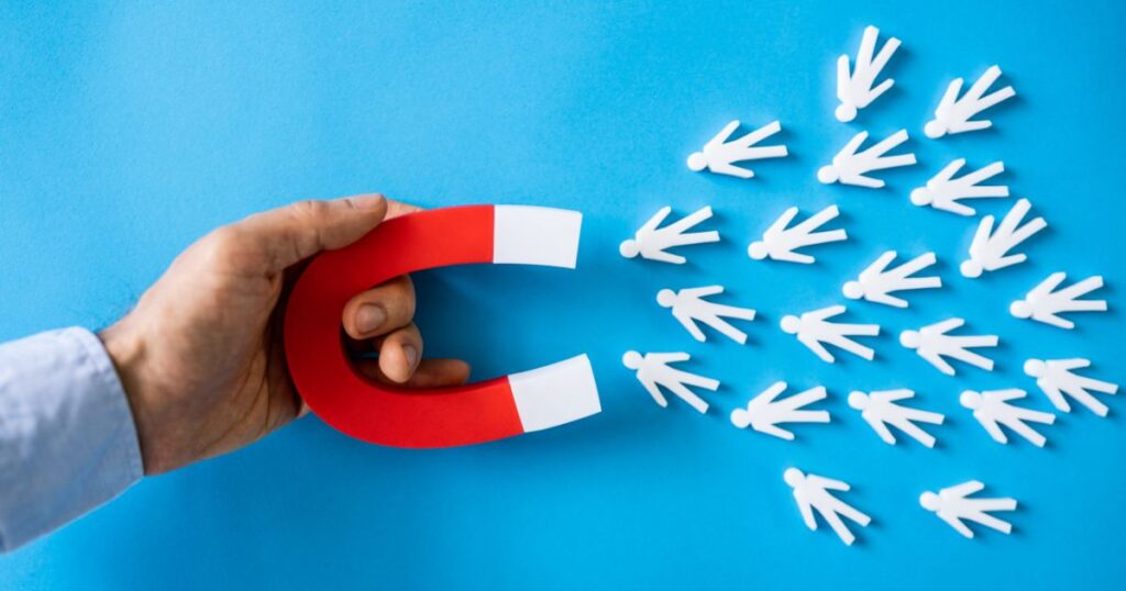 Closeup of a man's hand holding a red and white u-magnet that appears to be attracting small people cutouts.