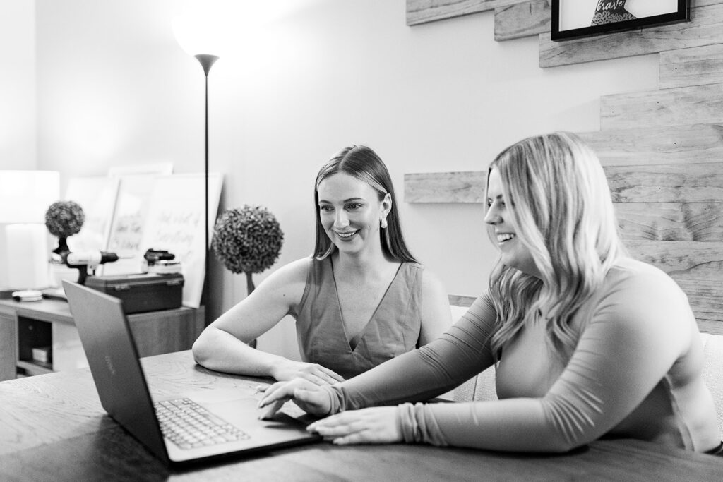 Two women laughing as they look over information on a laptop screen.