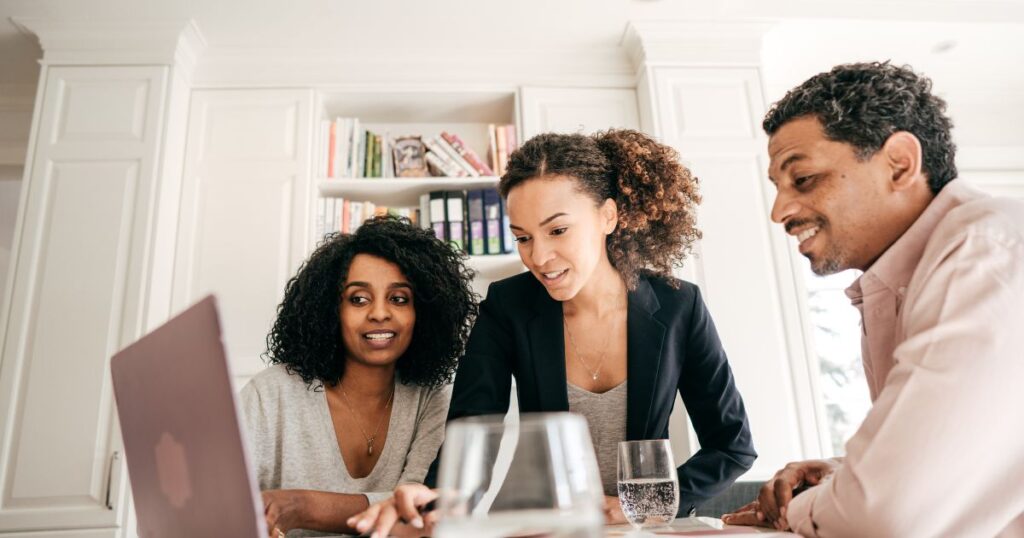 Two women and a man looking at information on a laptop screen.
